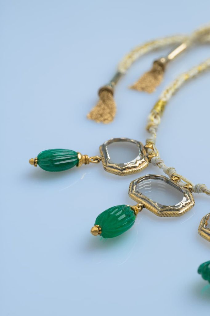 Braided cord, gold-wire tassels, and carved emerald drops of the necklace.